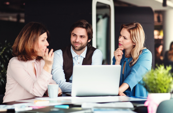 A group of cheerful business people sitting in an office, using laptop.