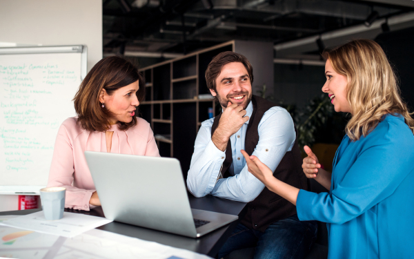 A group of cheerful business people sitting in an office, using laptop.