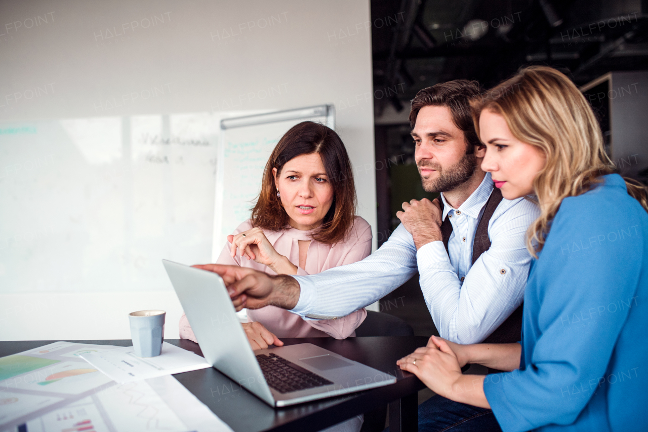 A group of cheerful business people sitting in an office, using laptop.