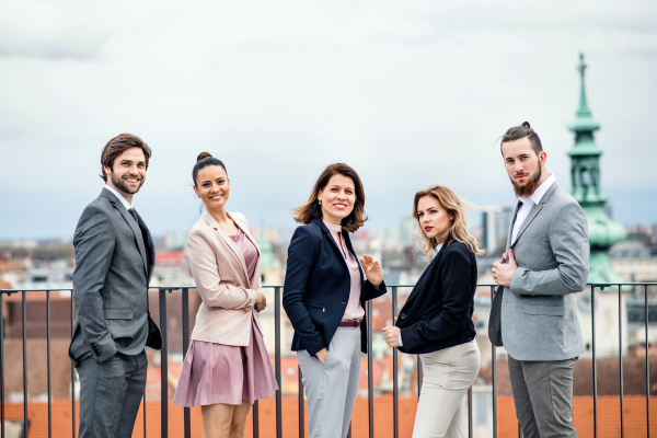 A front view portrait of group of joyful businesspeople standing outdoors on roof terrace in city.