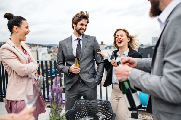 A large group of joyful businesspeople having a party outdoors on roof terrace in city.