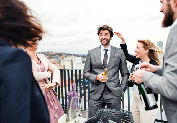 A large group of joyful businesspeople having a party outdoors on roof terrace in city.