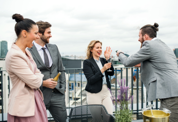 A large group of joyful businesspeople having a party outdoors on roof terrace in city.