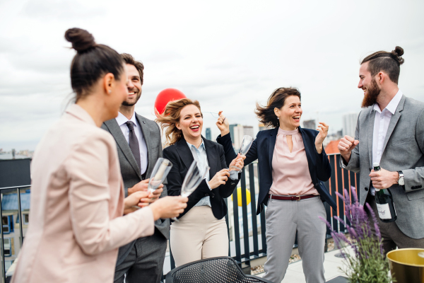 A large group of joyful businesspeople having a party outdoors on roof terrace in city.