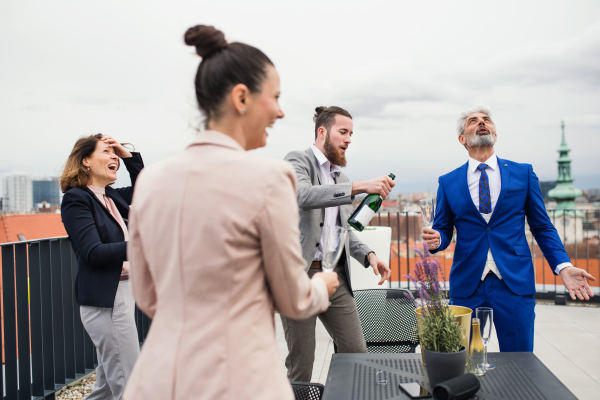 A large group of joyful businesspeople having a party outdoors on roof terrace in city.