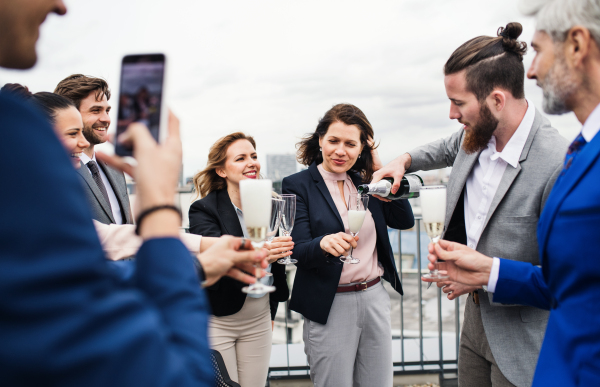 A large group of joyful businesspeople having a party outdoors on roof terrace in city, taking a photo.