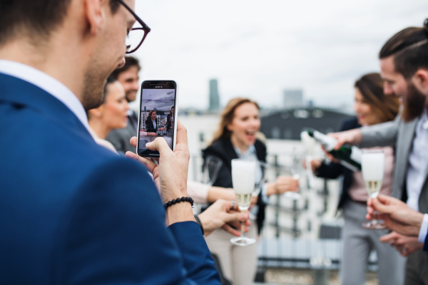 A large group of joyful businesspeople having a party outdoors on roof terrace in city, taking a photo.