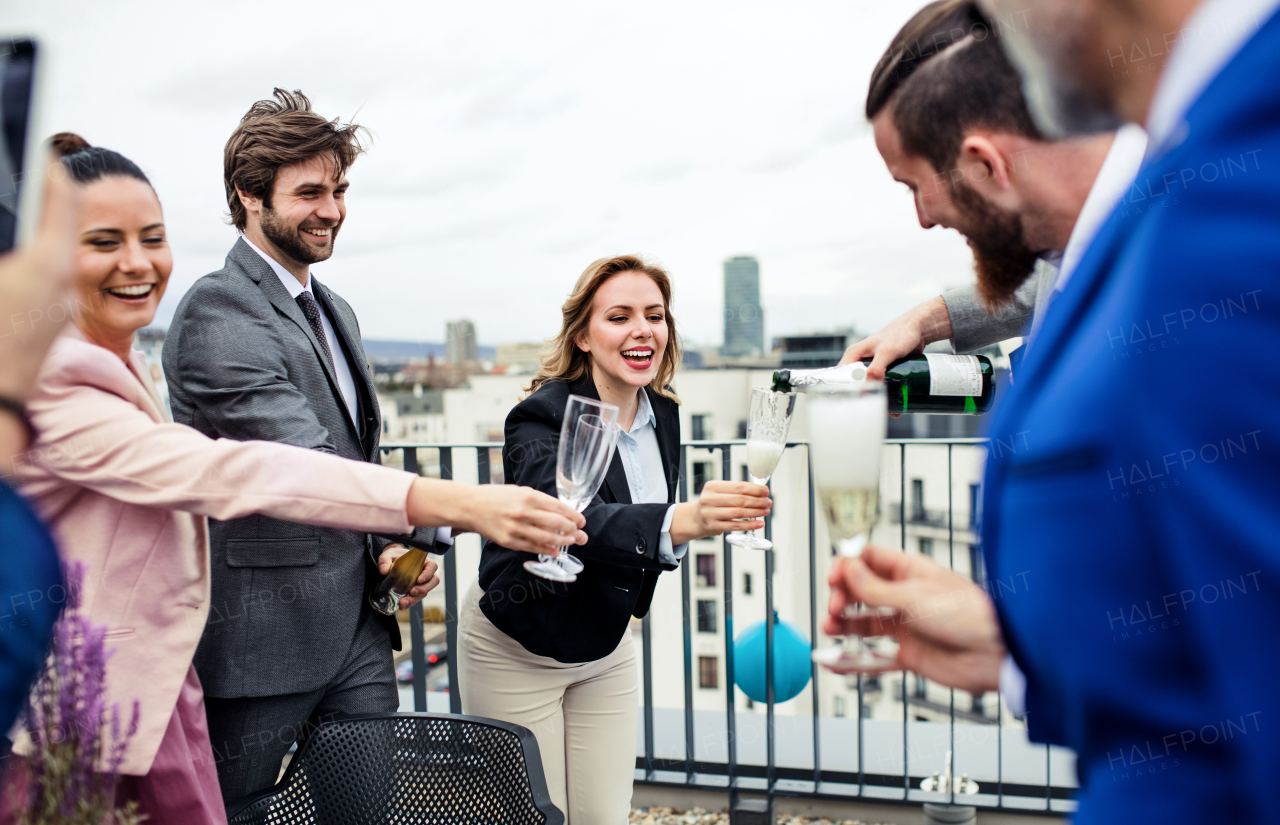 A large group of joyful businesspeople having a party outdoors on roof terrace in city, taking a photo.