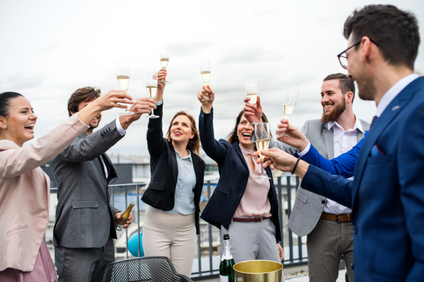 A large group of joyful businesspeople having a party outdoors on roof terrace in city.