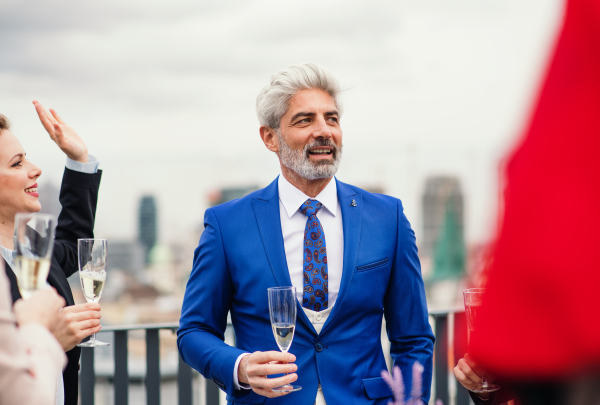 A mature businessman with colleagues having a party outdoors on roof terrace in city.