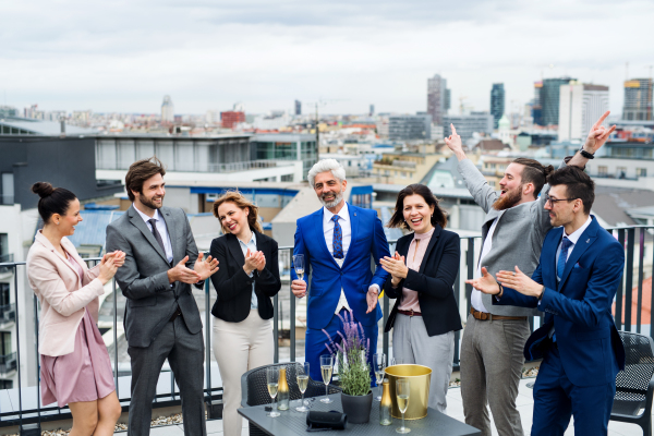 A large group of joyful businesspeople having a party outdoors on roof terrace in city.