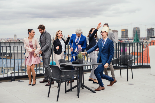 A large group of joyful businesspeople having a party outdoors on roof terrace in city.