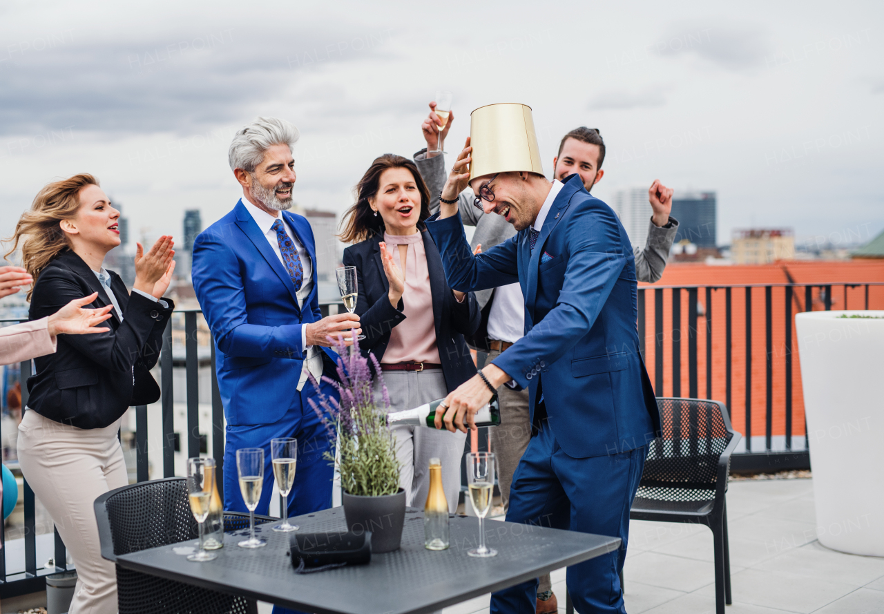 A large group of joyful businesspeople having a party outdoors on roof terrace in city, pouring champagne.