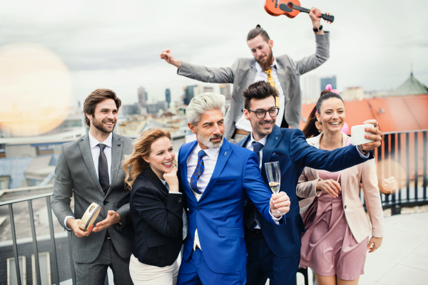 A large group of joyful businesspeople having a party outdoors on roof terrace in city.