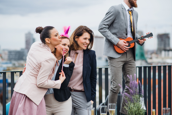 A large group of joyful businesspeople having a party outdoors on roof terrace in city, posing for a photo.