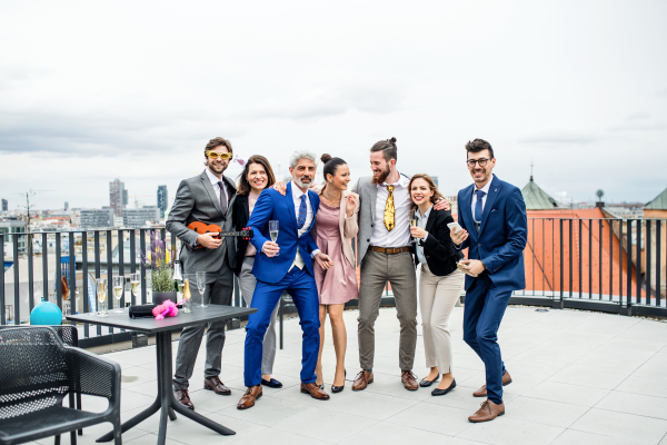 A portrait of large group of joyful businesspeople having a party outdoors on roof terrace in city.