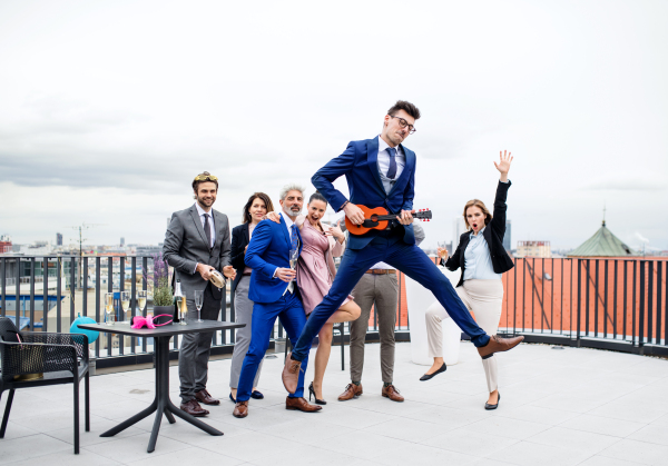 A large group of joyful businesspeople having a party outdoors on roof terrace in city.