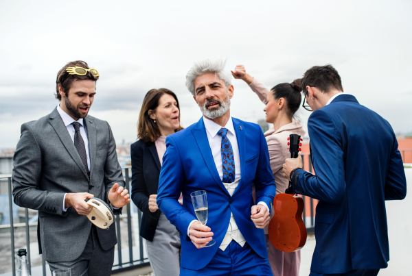 A large group of joyful businesspeople having a party outdoors on roof terrace in city, dancing.