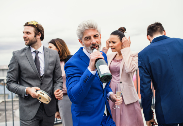 A large group of joyful businesspeople having a party outdoors on roof terrace in city.