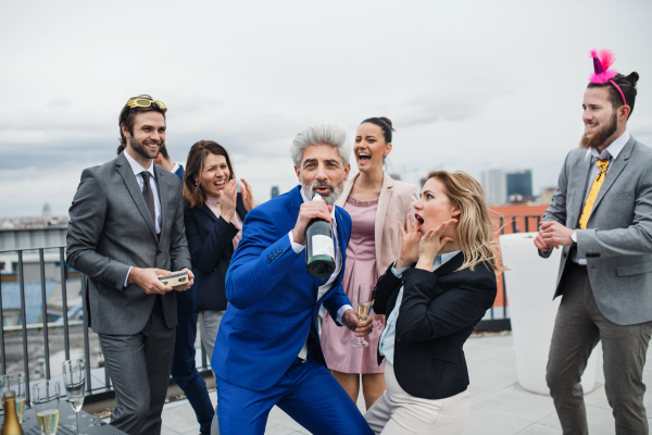 A large group of joyful businesspeople having a party outdoors on roof terrace in city.