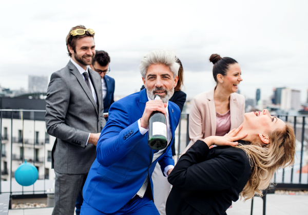 A large group of joyful businesspeople having a party outdoors on roof terrace in city.