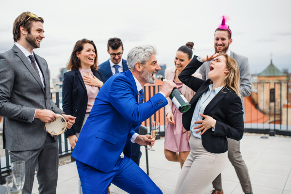 A large group of joyful businesspeople having a party outdoors on roof terrace in city.