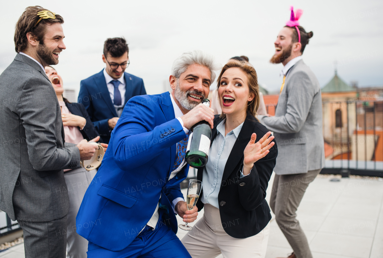 A large group of joyful businesspeople having a party outdoors on roof terrace in city.