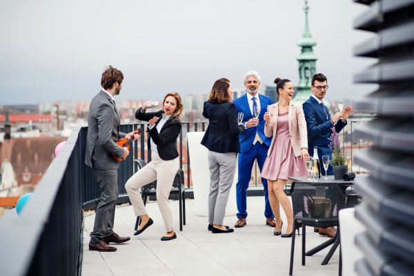 A large group of joyful businesspeople having a party outdoors on roof terrace in city.