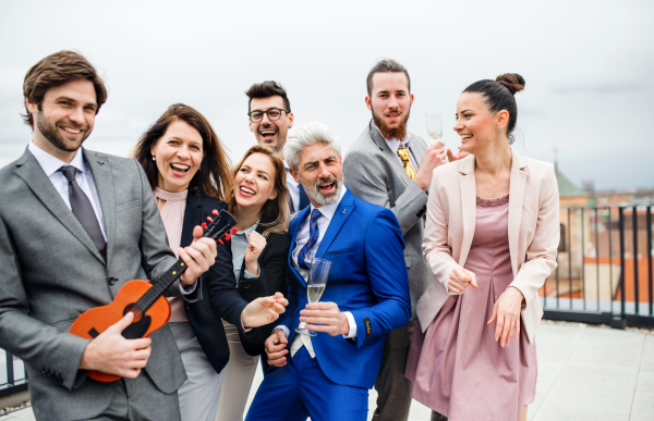 A large group of joyful businesspeople having a party outdoors on roof terrace in city.