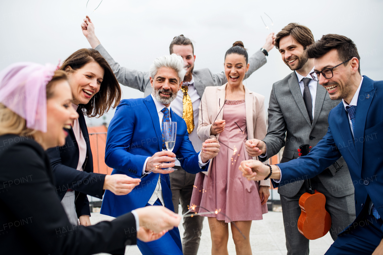 A large group of joyful businesspeople with sparklers having a party outdoors on roof terrace in city.