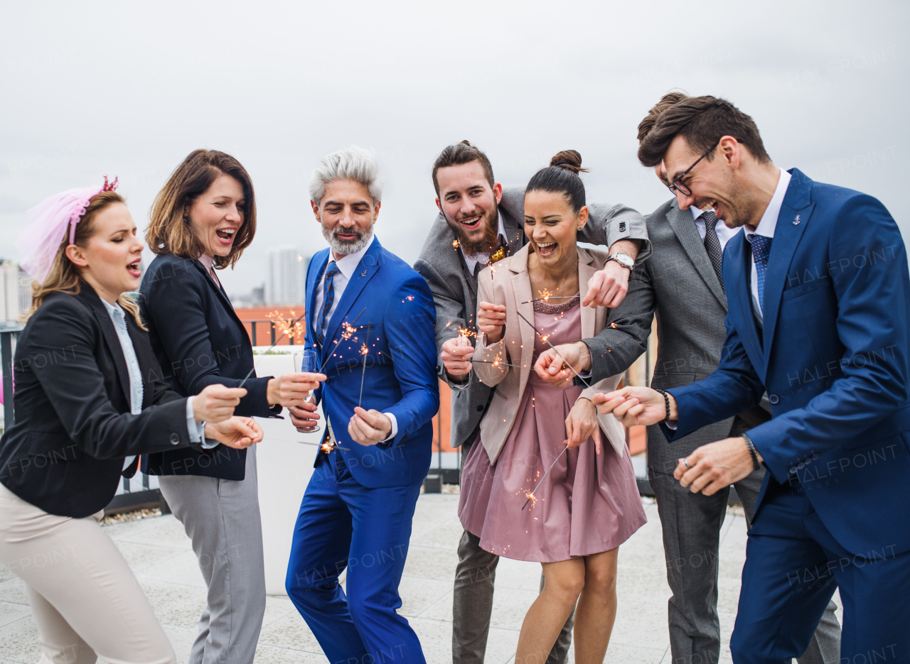 A large group of joyful businesspeople with sparklers having a party outdoors on roof terrace in city.