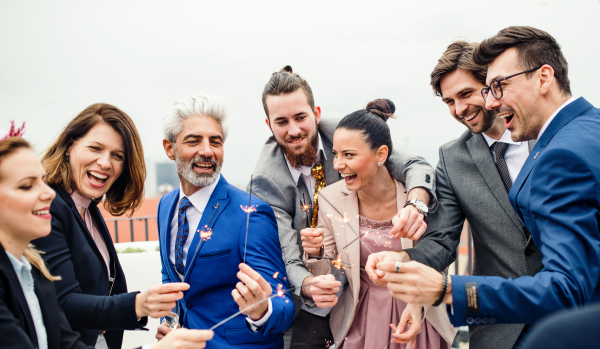 A large group of joyful businesspeople having a party outdoors on roof terrace in city, holding sparklers.