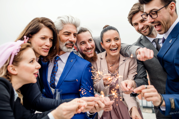 A large group of joyful businesspeople with sparklers having a party outdoors on roof terrace in city.