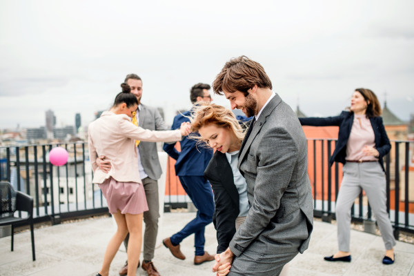 A large group of joyful businesspeople having a party outdoors on roof terrace in city, dancing.