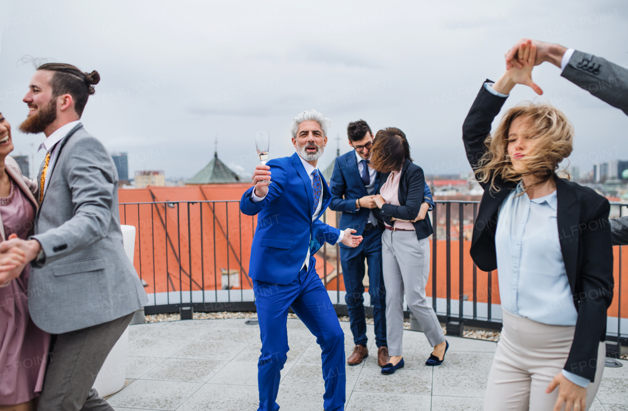 A large group of joyful businesspeople having a party outdoors on roof terrace in city, dancing.