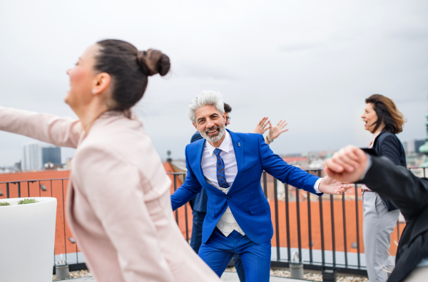 A large group of joyful businesspeople having a party outdoors on roof terrace in city, dancing.