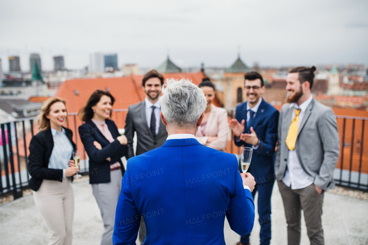 A portrait of large group of joyful businesspeople having a party outdoors on roof terrace in city.