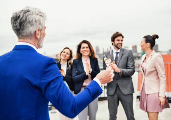 A large group of joyful businesspeople having a party outdoors on roof terrace in city.