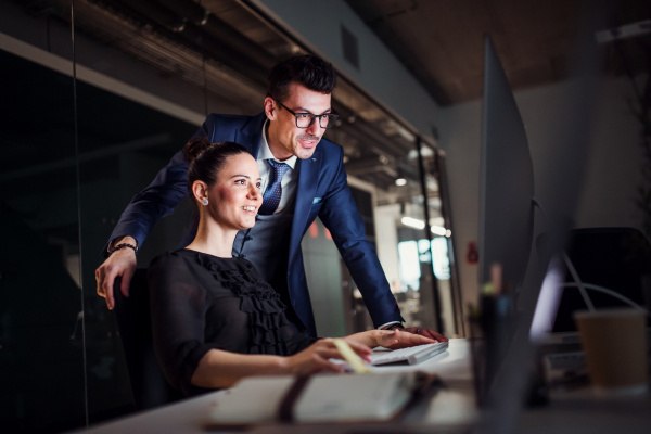 Two young business people in an office in the evening or at night, using computer.