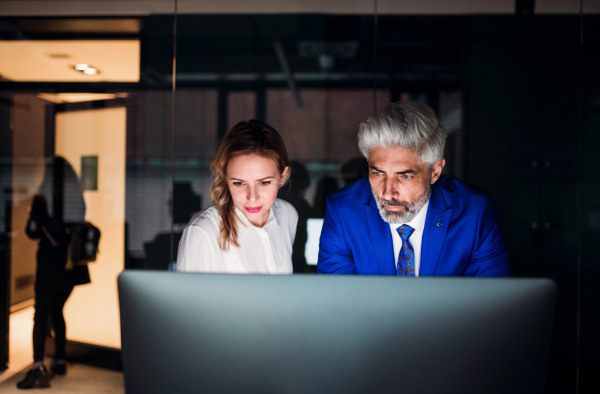 Front viewof two serious business people in an office at night, working.