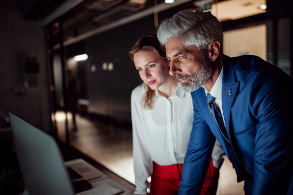 Two young business people in an office in the evening or at night, using computer.