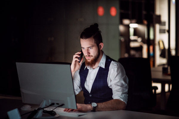 A portrait of young businessman with computer and smartphone in an office, working.