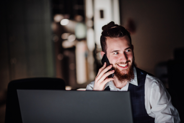 A portrait of young businessman with computer and smartphone in an office, working.