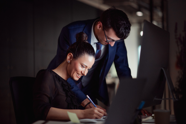 Two young business people in an office in the evening or at night, using computer.