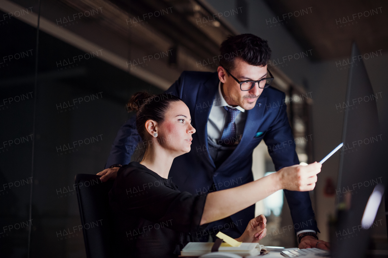 Two young business people in an office in the evening or at night, using computer.