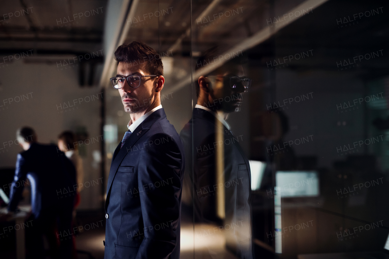 A portrait of young businessman standing in an office, in the evening. Copy space.