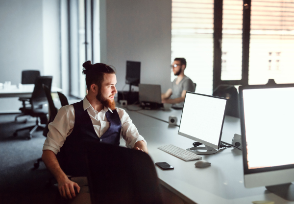 A portrait of young businessman sitting at the table in an office, working. Copy space.