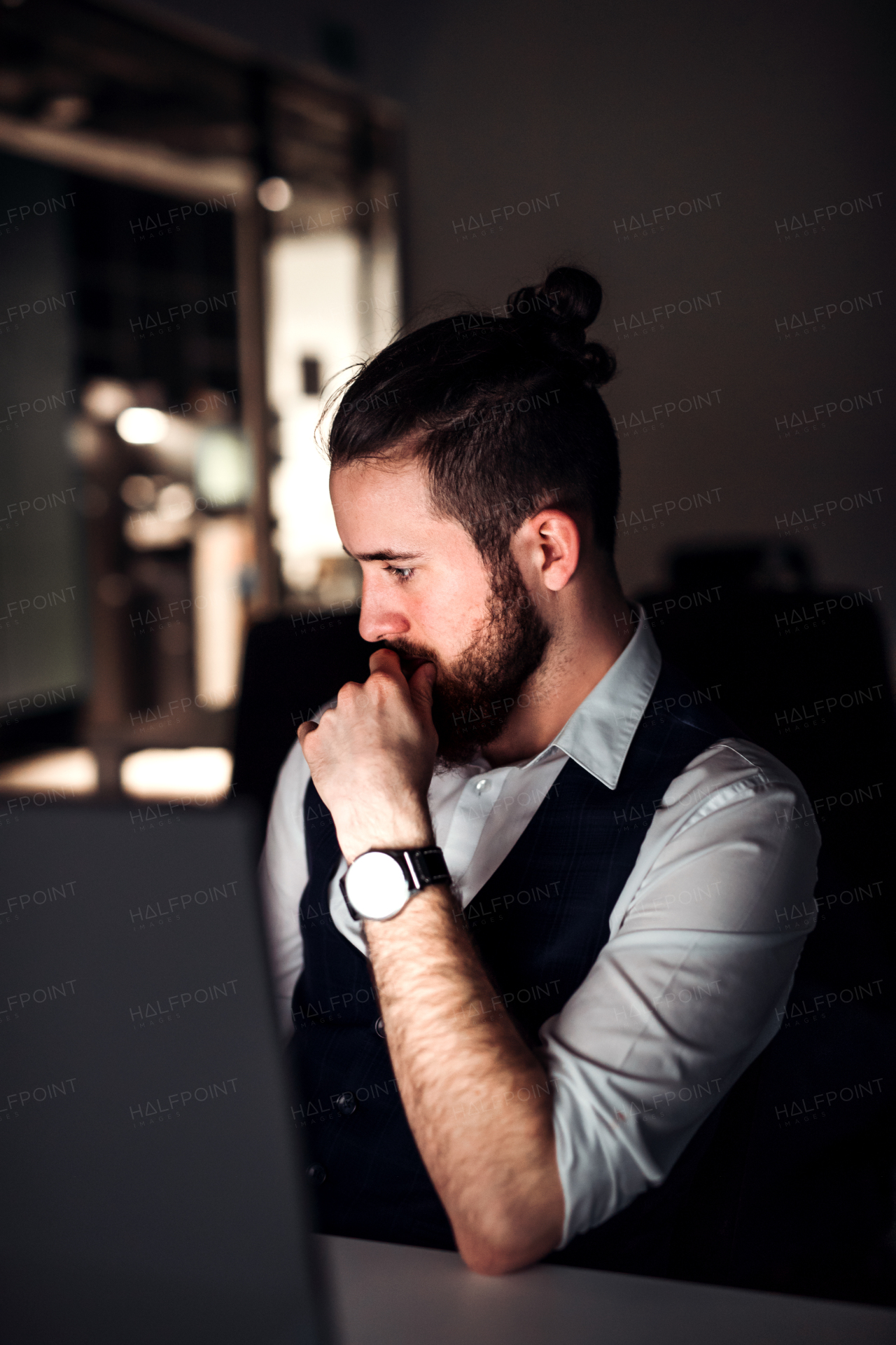 A portrait of young hipster businessman with computer in an office, working.