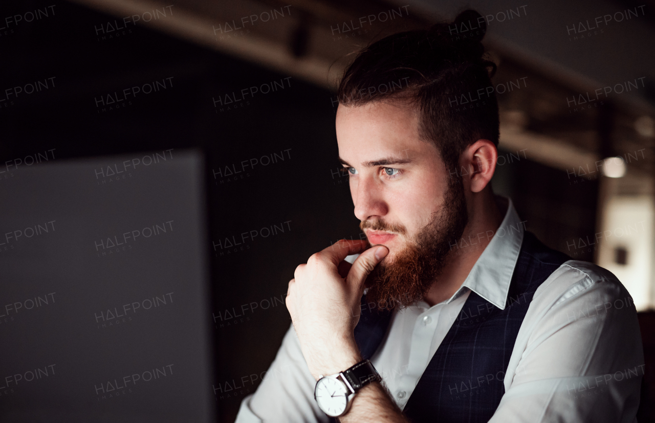 A portrait of young businessman in an office at night, working. Copy space.