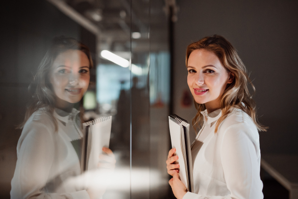 A portrait of young businesswoman with documents in an office, looking at camera.